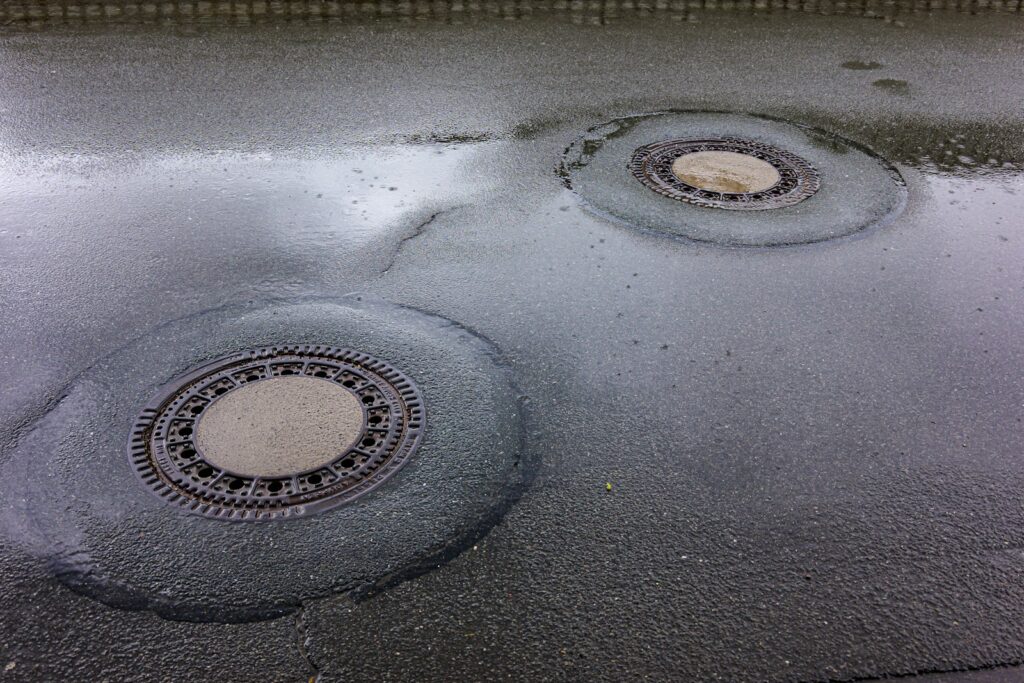 Rioolputdeksel in een natte straat na regen