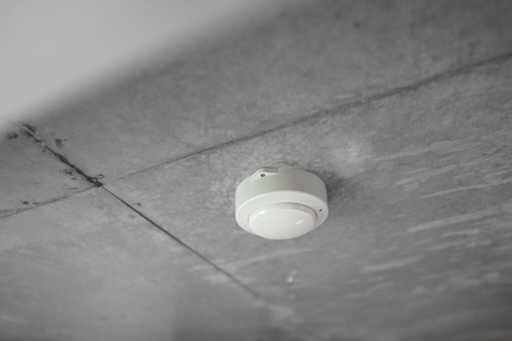 Hand die de testknop van een rookmelder aan het plafond indrukt
